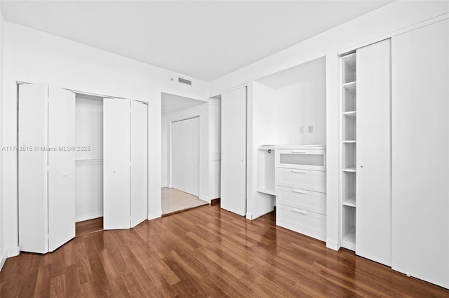 unfurnished bedroom featuring dark wood-style floors, visible vents, and two closets