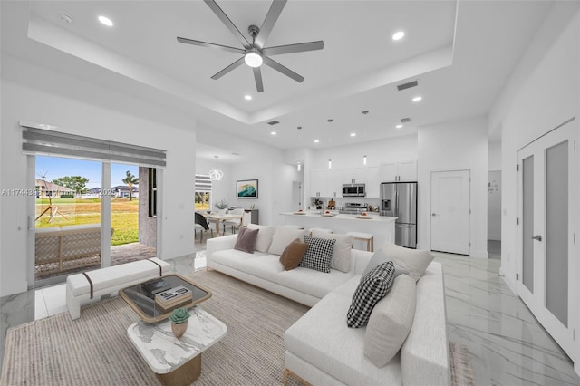 living room with ceiling fan, a tray ceiling, and a high ceiling