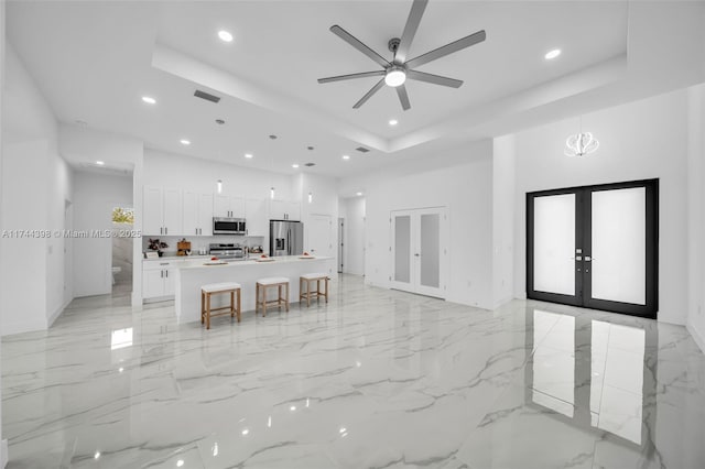 kitchen with appliances with stainless steel finishes, white cabinetry, an island with sink, a tray ceiling, and french doors