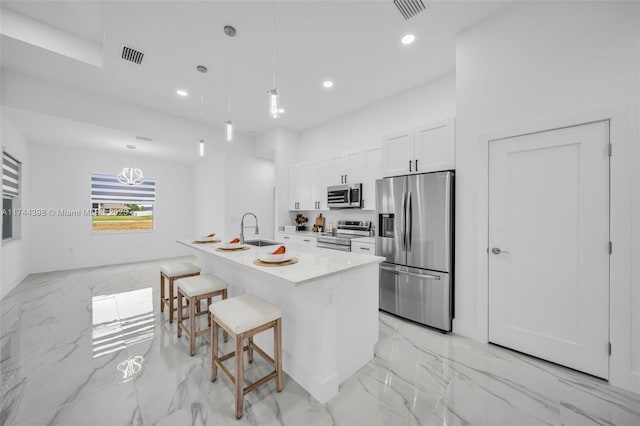 kitchen featuring sink, white cabinetry, appliances with stainless steel finishes, pendant lighting, and a kitchen island with sink