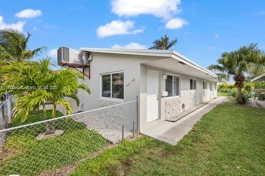 rear view of house with stucco siding, a yard, and fence