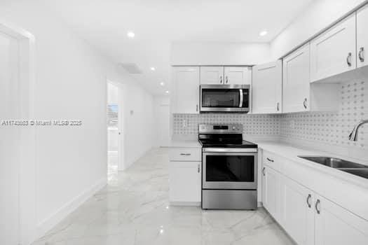 1431-1433 N 14th Way, Hollywood, FL 33020 - kitchen featuring stainless steel appliances, light marble finish flooring, white cabinetry, backsplash, and light countertops