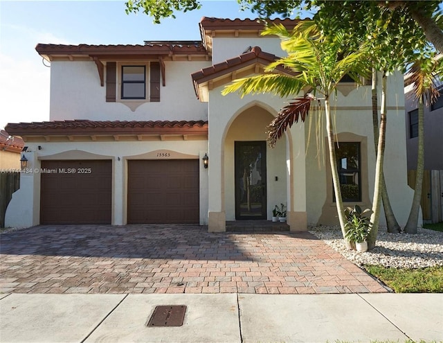 mediterranean / spanish house with an attached garage, decorative driveway, and stucco siding