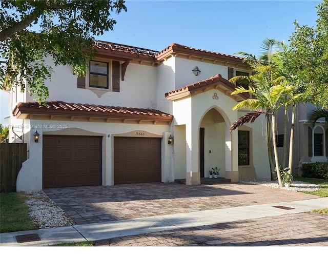 mediterranean / spanish house with a garage, a tile roof, decorative driveway, and stucco siding