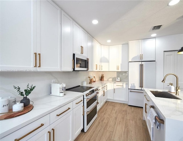 kitchen with high quality appliances, visible vents, white cabinets, and a sink