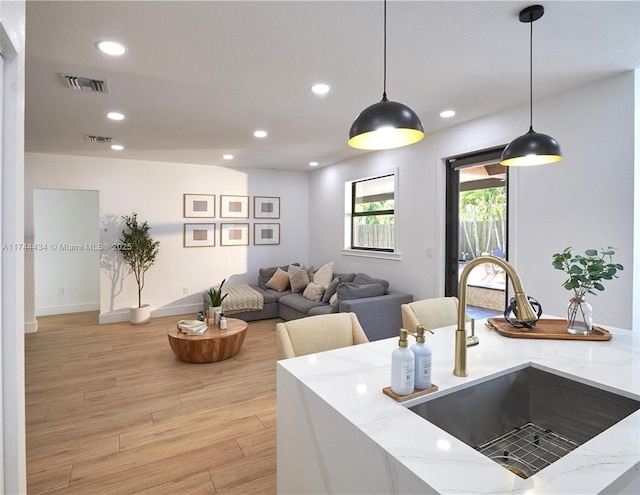 kitchen with light stone countertops, pendant lighting, a sink, and light wood finished floors