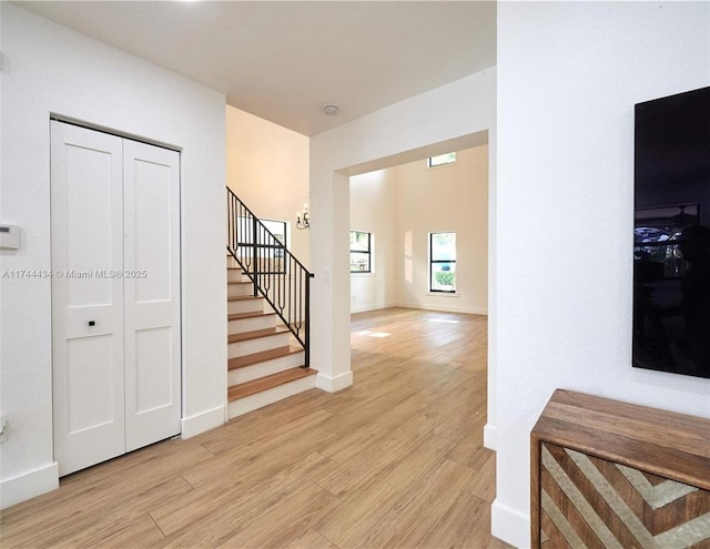 hallway with light wood-type flooring, stairs, and baseboards