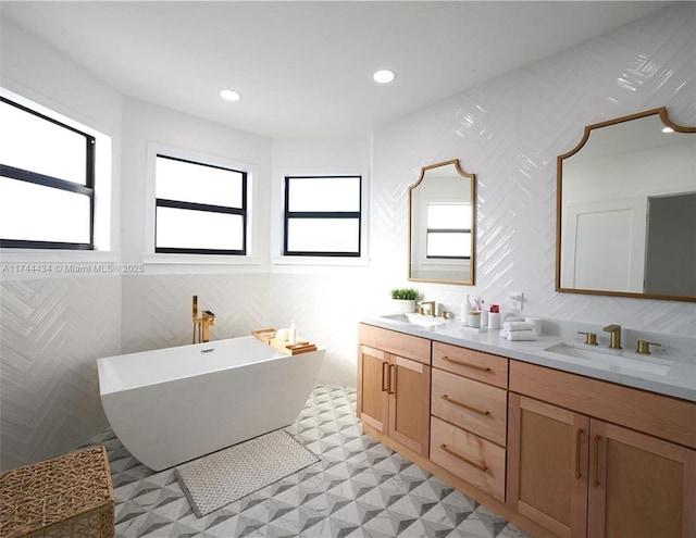 bathroom featuring double vanity, a freestanding tub, a sink, and recessed lighting