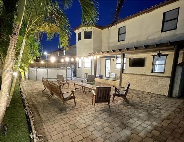 patio at night featuring fence and a ceiling fan