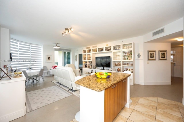 kitchen with visible vents, light stone counters, a kitchen island, open floor plan, and light tile patterned floors
