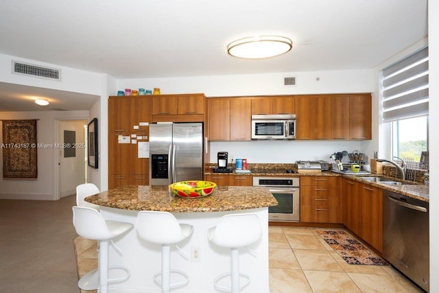 kitchen with a kitchen island, stone countertops, sink, a breakfast bar area, and stainless steel appliances