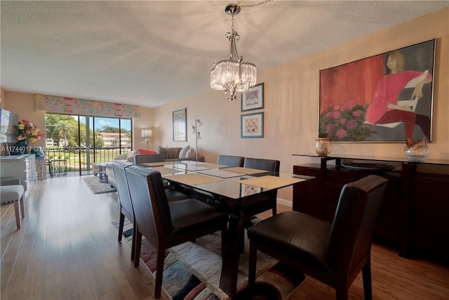 dining space with a textured ceiling, an inviting chandelier, and light wood-style floors