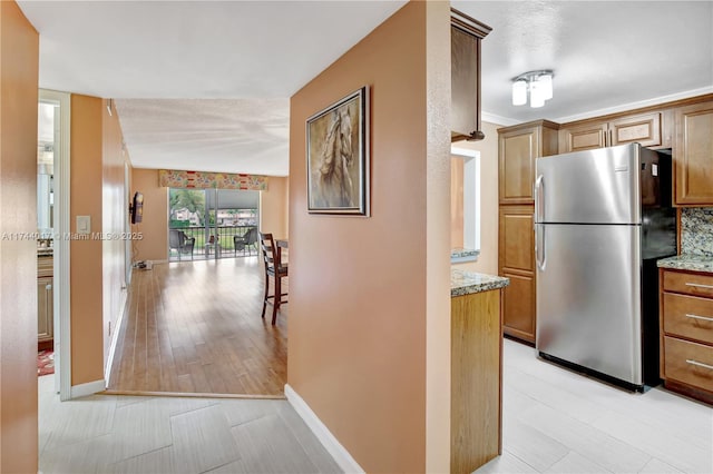 kitchen with light stone counters, freestanding refrigerator, brown cabinets, and baseboards