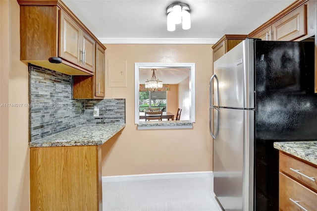 kitchen with a notable chandelier, backsplash, freestanding refrigerator, and light stone countertops