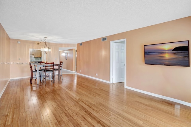 dining room featuring a textured ceiling, visible vents, baseboards, light wood-style floors, and an inviting chandelier