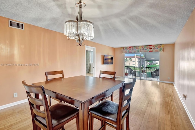 dining space featuring light wood-style floors, visible vents, a textured ceiling, and baseboards