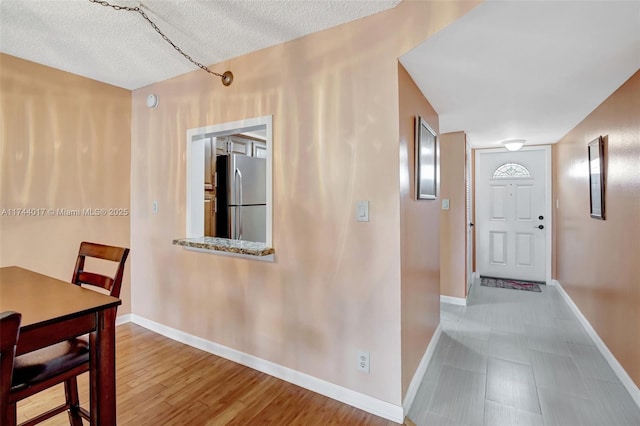 hall featuring a textured ceiling, light wood-style floors, and baseboards