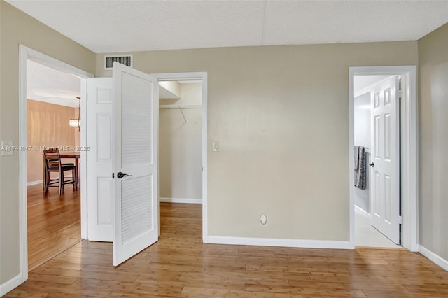 unfurnished bedroom with light wood-style floors, baseboards, visible vents, and a textured ceiling