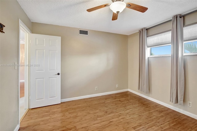 unfurnished room featuring light wood-type flooring, visible vents, a textured ceiling, and baseboards