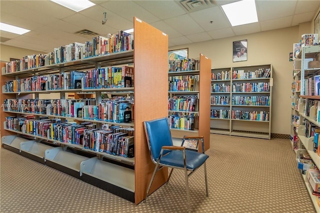 living area with carpet, visible vents, and wall of books