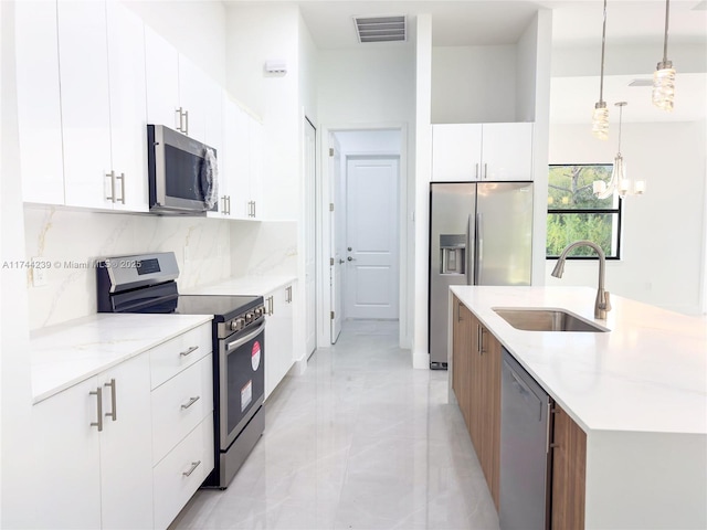 kitchen with pendant lighting, tasteful backsplash, sink, white cabinets, and stainless steel appliances