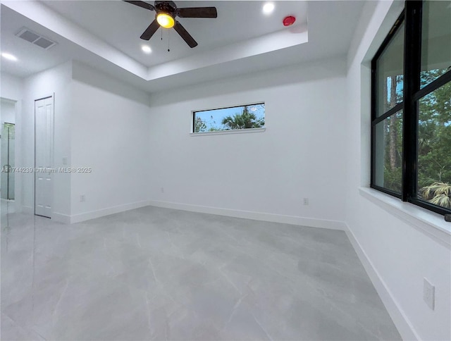 empty room featuring ceiling fan and a tray ceiling