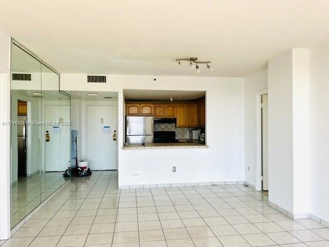 kitchen with tasteful backsplash, tile counters, stainless steel fridge, and light tile patterned floors