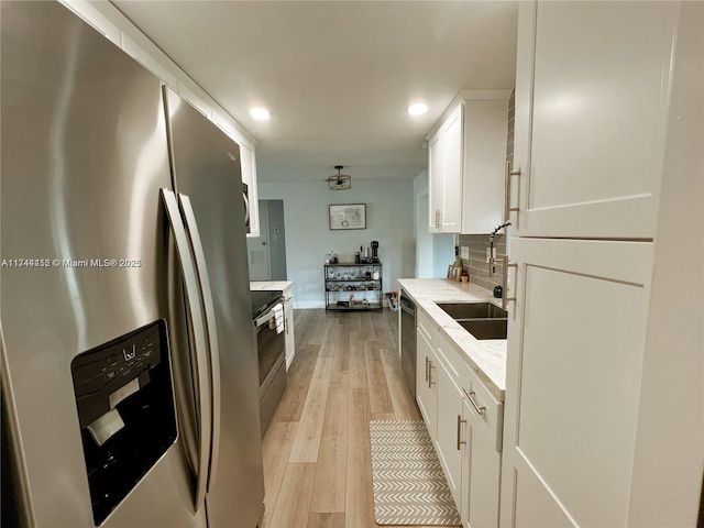 kitchen featuring sink, white cabinetry, light wood-type flooring, stainless steel appliances, and decorative backsplash