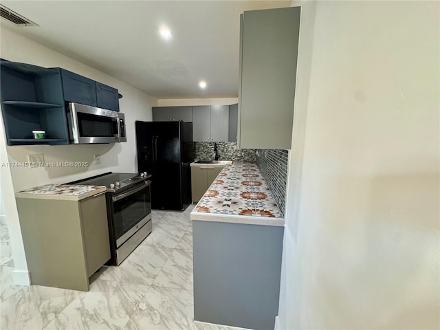 kitchen with appliances with stainless steel finishes, a sink, marble finish floor, gray cabinets, and backsplash