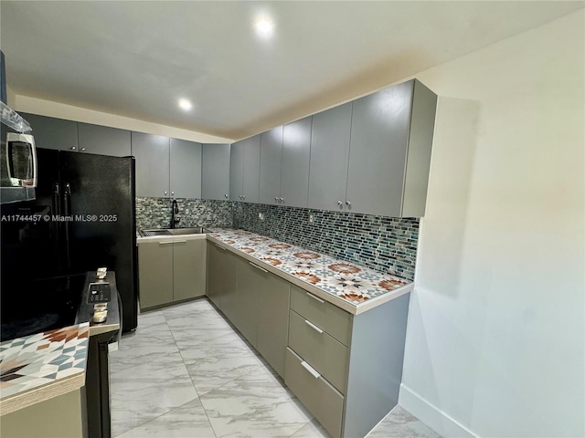 kitchen with marble finish floor, tasteful backsplash, gray cabinetry, freestanding refrigerator, and a sink