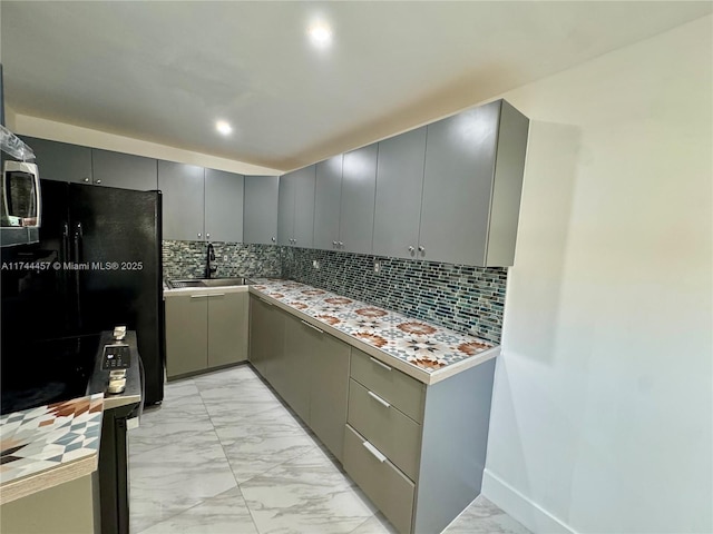 kitchen with marble finish floor, gray cabinets, a sink, and freestanding refrigerator