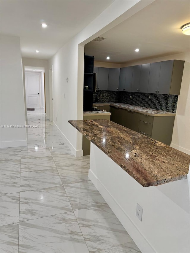 kitchen with dark stone counters, marble finish floor, backsplash, and gray cabinetry