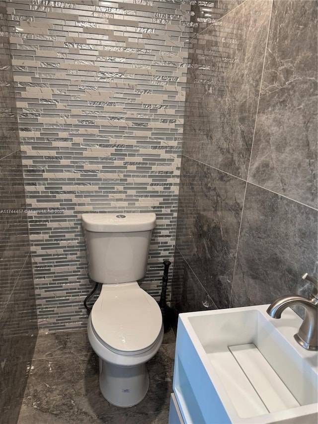 bathroom with toilet, tile walls, and a sink