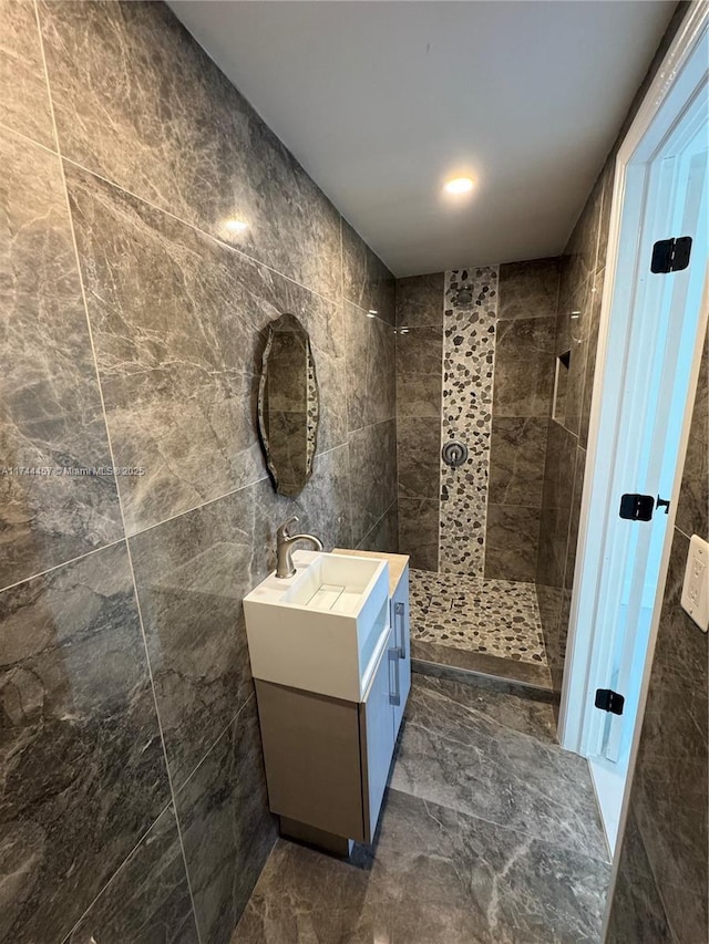 full bathroom with marble finish floor, a tile shower, vanity, and tile walls