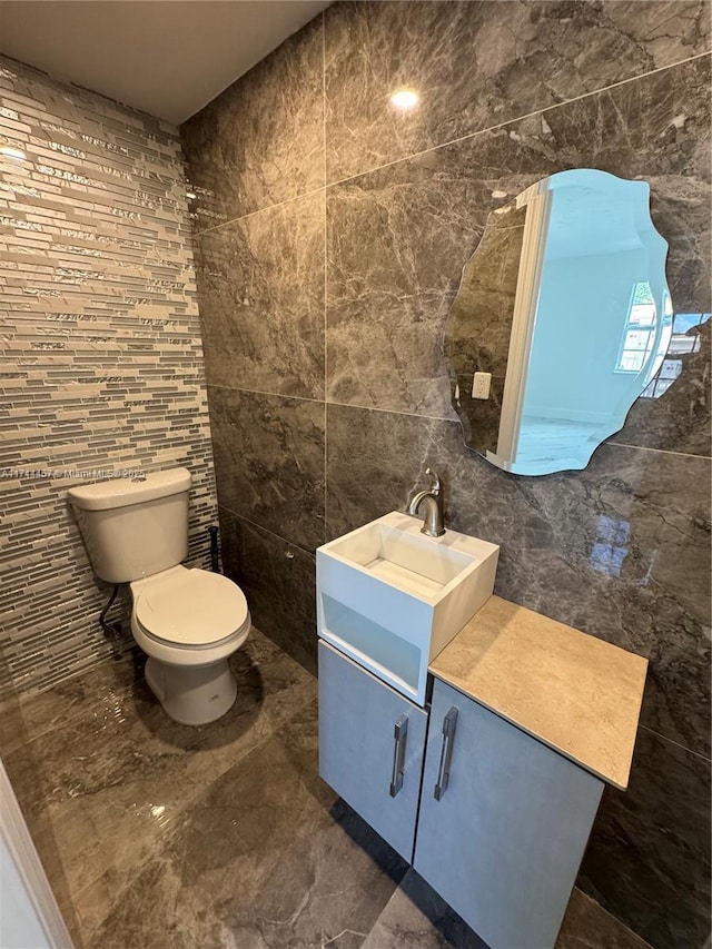 bathroom with marble finish floor, vanity, toilet, and tile walls