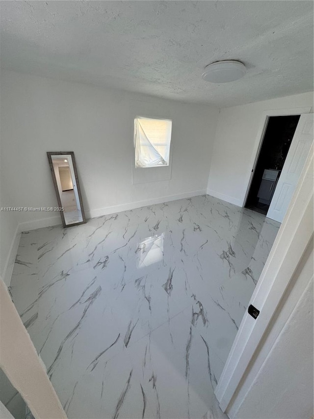 unfurnished room featuring a textured ceiling, marble finish floor, and baseboards