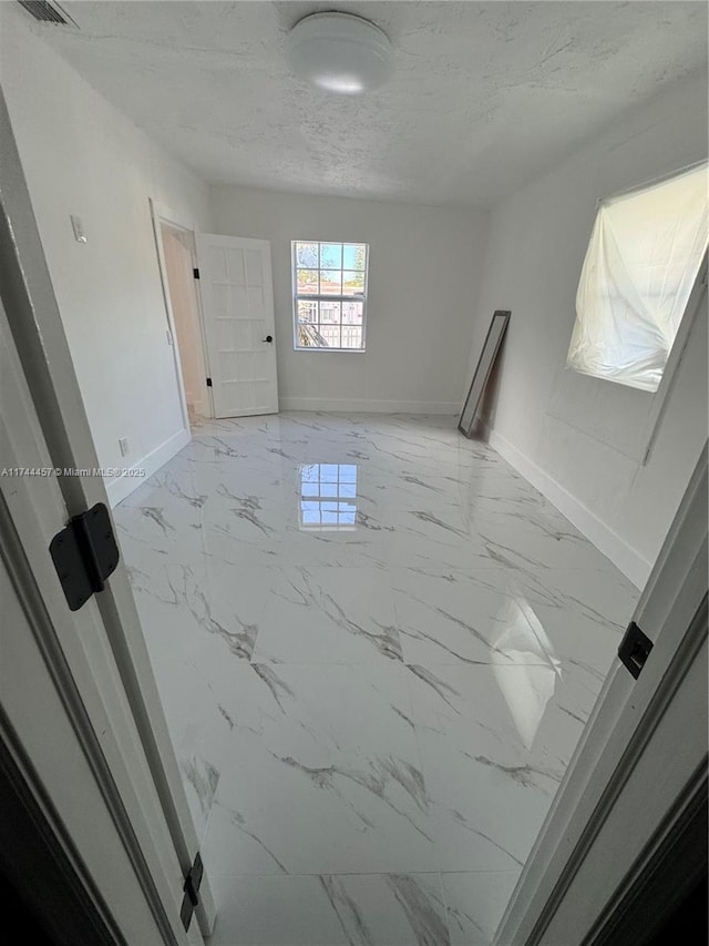 spare room featuring marble finish floor, visible vents, baseboards, and a textured ceiling