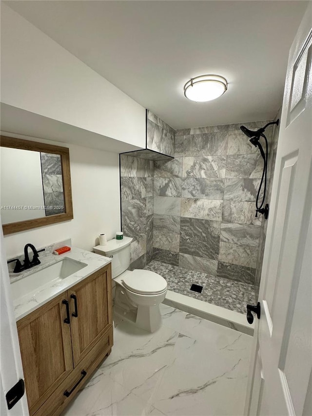 bathroom featuring toilet, marble finish floor, a tile shower, and vanity