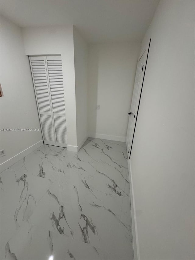 unfurnished bedroom with marble finish floor, baseboards, and a closet