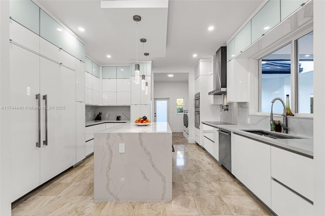 kitchen featuring pendant lighting, wall chimney range hood, sink, white cabinets, and a kitchen island