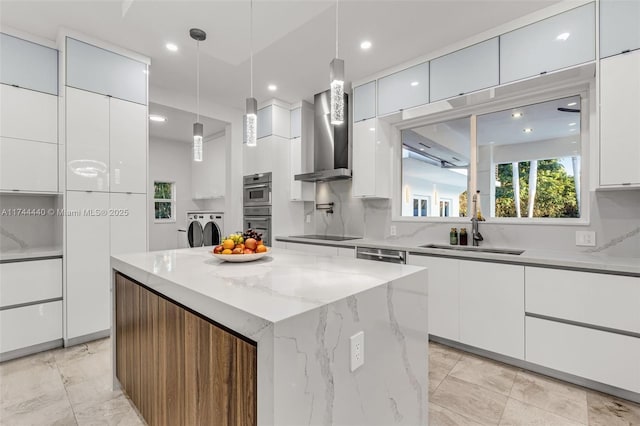 kitchen featuring a kitchen island, pendant lighting, white cabinets, washing machine and clothes dryer, and wall chimney range hood