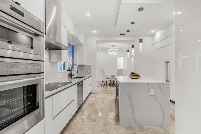 kitchen with sink, appliances with stainless steel finishes, white cabinets, a kitchen island, and decorative light fixtures