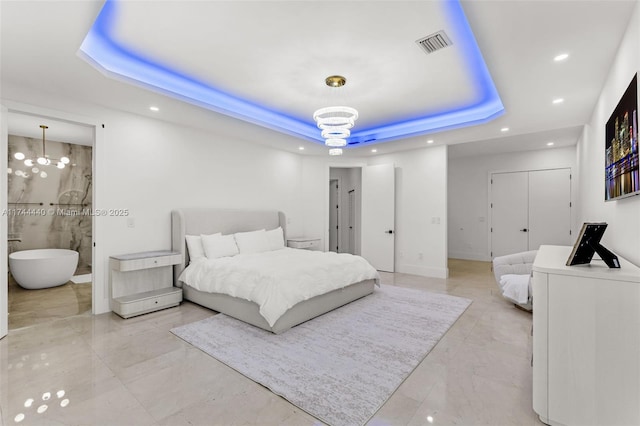 bedroom featuring connected bathroom, an inviting chandelier, and a tray ceiling