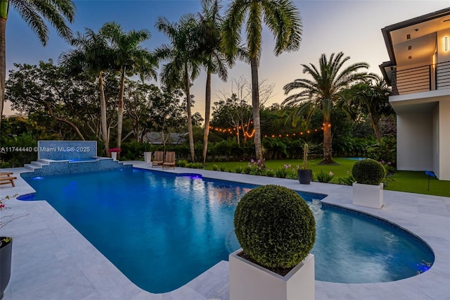 pool at dusk with a patio area and pool water feature