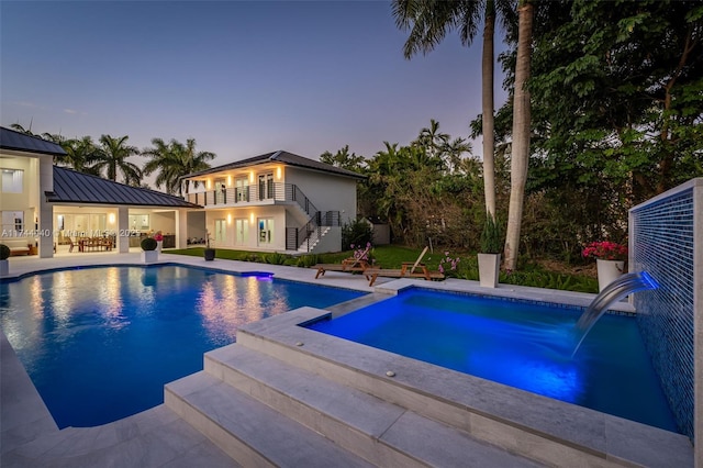 pool at dusk with pool water feature and a patio area