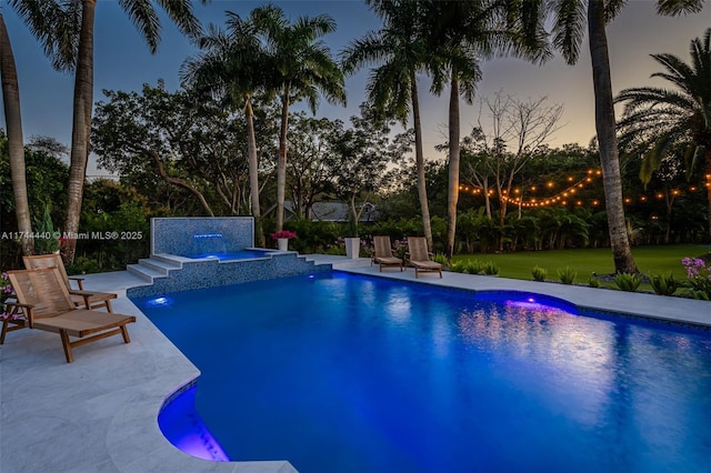 pool at dusk featuring pool water feature, a hot tub, and a patio area