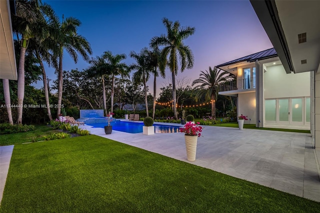 yard at dusk featuring a patio area, pool water feature, and a balcony