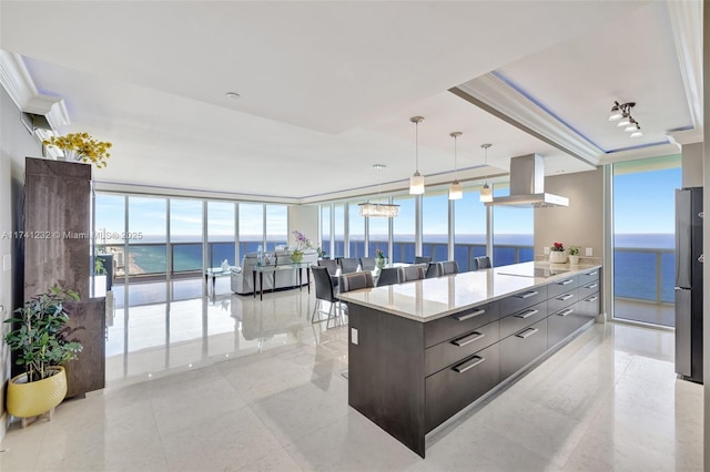 kitchen featuring a water view, decorative light fixtures, a wall of windows, stainless steel refrigerator, and island exhaust hood