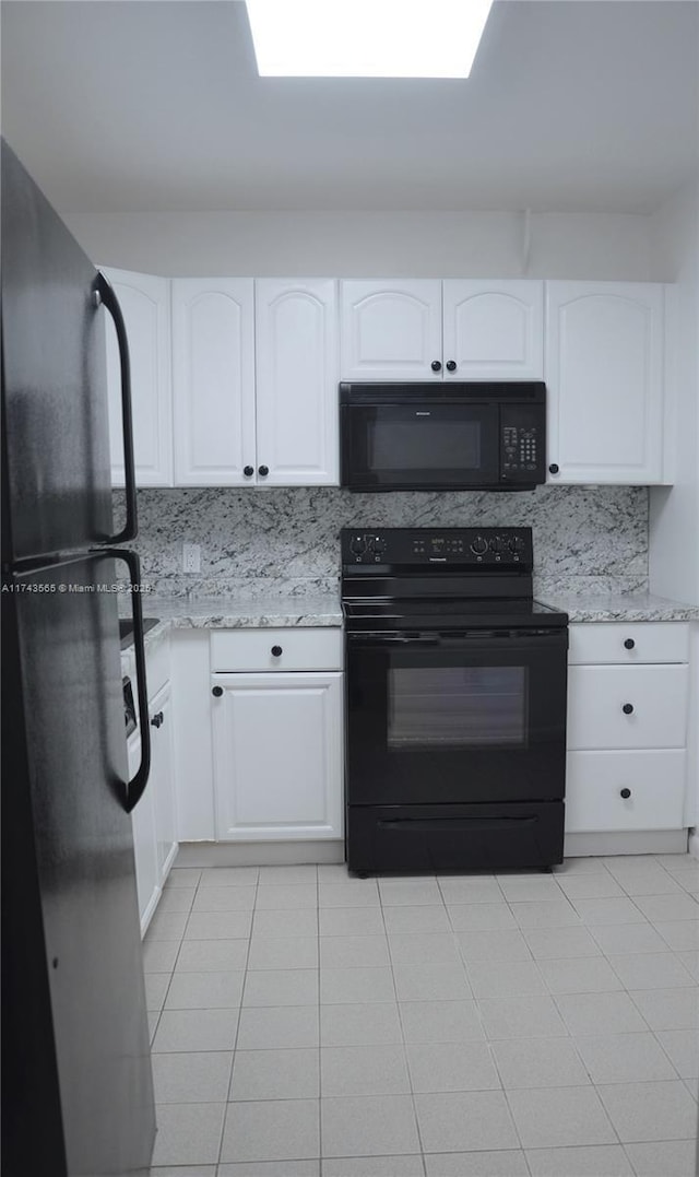 kitchen with white cabinetry, backsplash, light stone counters, and black appliances