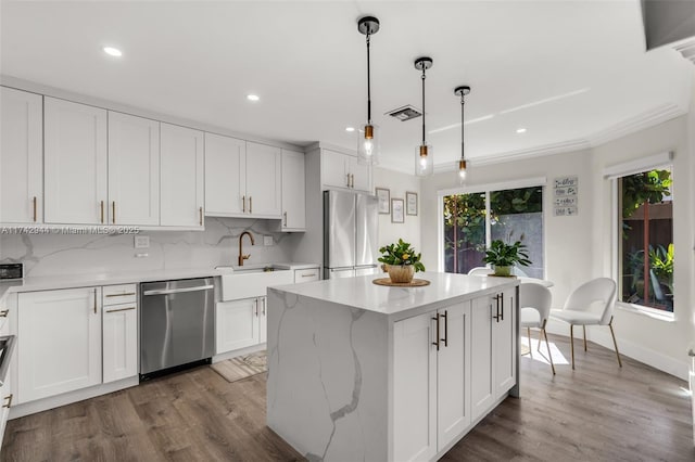 kitchen with sink, appliances with stainless steel finishes, white cabinetry, a center island, and decorative light fixtures